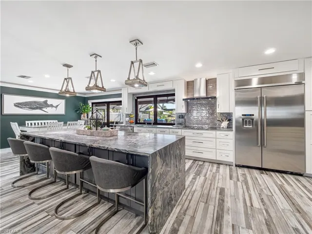 Kitchen featuring a breakfast bar area, dark stone counters, stainless steel built in refrigerator, hanging light fixtures, and a large island