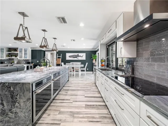Kitchen with backsplash, two tone cabinets, dark stone counters, black electric stovetop, and stainless steel double oven