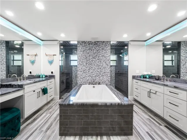 Bathroom with two vanities, a bath, tiled shower, and light wood finished floors