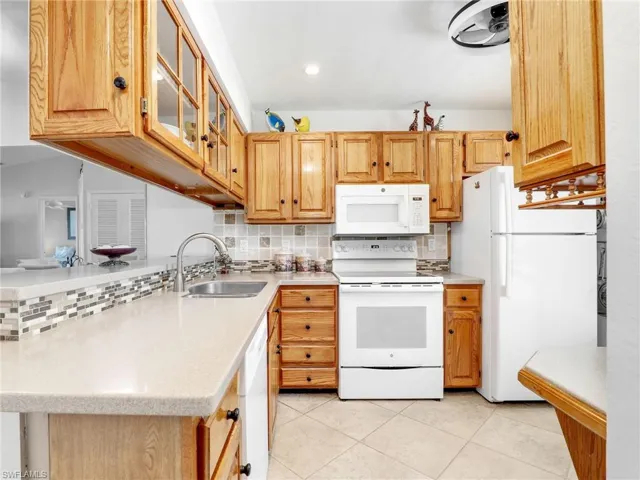 Kitchen with a sink, white appliances, backsplash, and light countertops