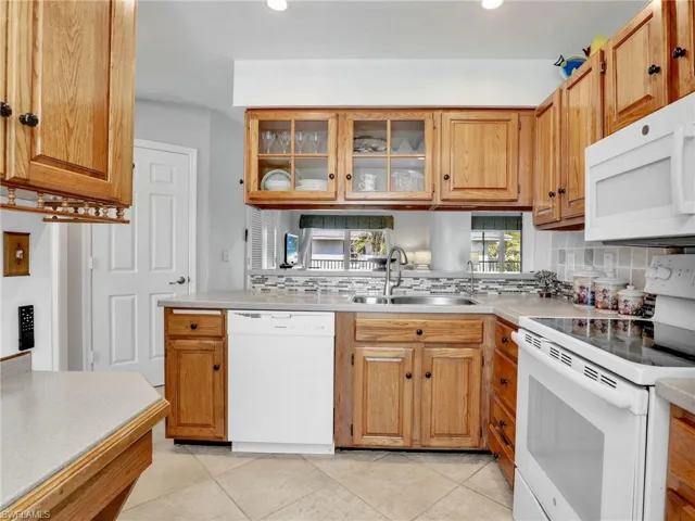Kitchen with a sink, white appliances, backsplash, and light countertops