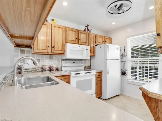 Kitchen with white appliances, a healthy amount of sunlight, backsplash, and a sink