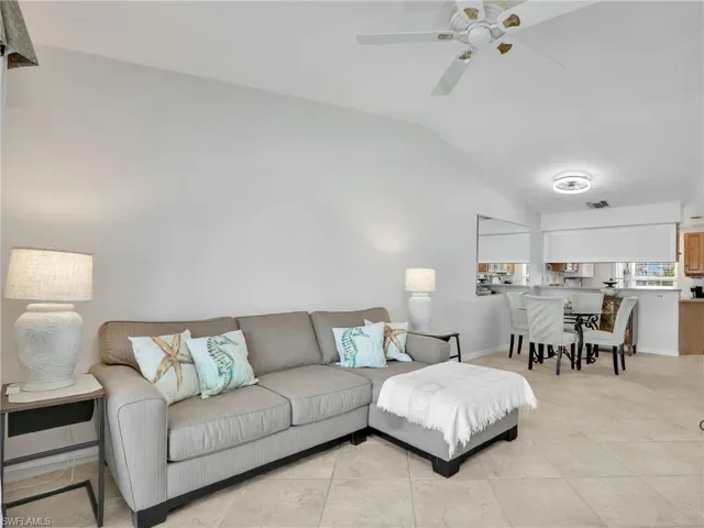 Living room featuring light tile patterned floors, visible vents, ceiling fan, and lofted ceiling