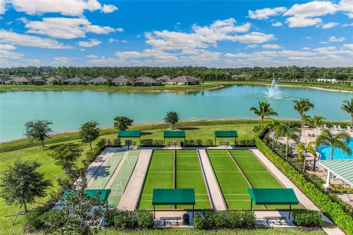 Expansive water feature with a fountain, surrounded by green lawns, palm trees, and recreational courts