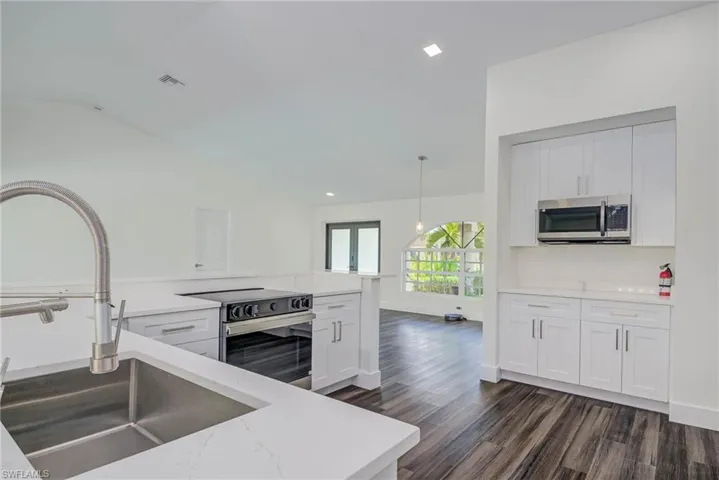 Kitchen featuring stainless steel appliances, a sink, dark wood-style floors, vaulted ceiling, and light stone counters