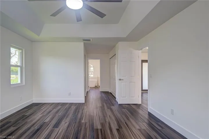 Empty room with a tray ceiling, dark wood-style floors, baseboards, and ceiling fan