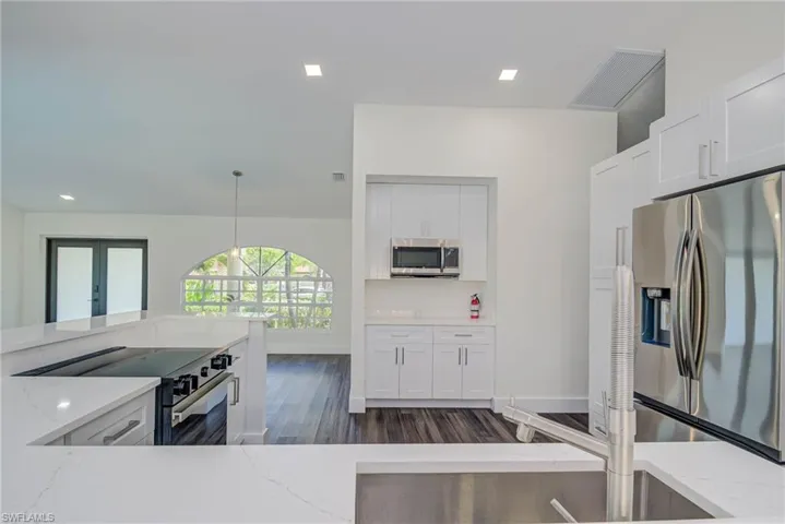 Kitchen featuring stainless steel appliances, light stone counters, dark wood finished floors, white cabinetry, and hanging light fixtures