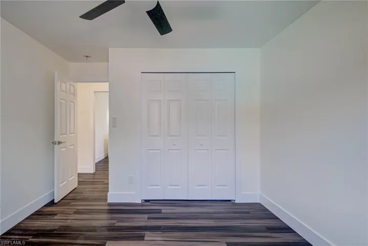 Unfurnished bedroom with dark wood-style floors, baseboards, a closet, and a ceiling fan