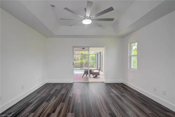 Empty room featuring a tray ceiling, plenty of natural light, ceiling fan, and baseboards
