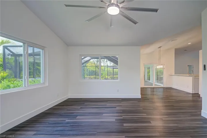 Unfurnished room with plenty of natural light, vaulted ceiling, a chandelier, and dark wood-style floors
