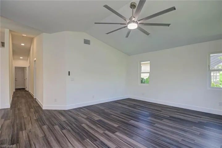 Unfurnished room with vaulted ceiling, dark wood finished floors, baseboards, and ceiling fan