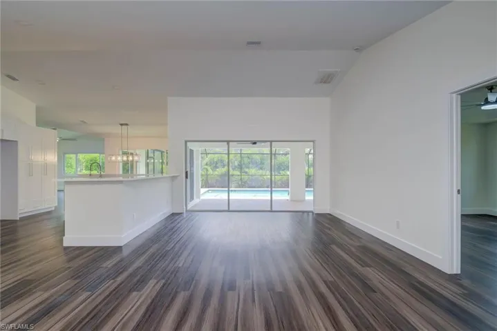 Unfurnished living room with dark wood-style flooring, baseboards, a sink, vaulted ceiling, and ceiling fan