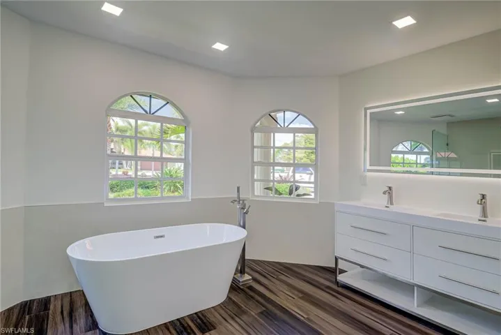 Full bathroom featuring double vanity, a freestanding tub, and wood finished floors