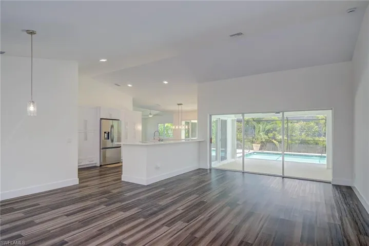 Unfurnished living room with dark wood finished floors, baseboards, vaulted ceiling, and recessed lighting