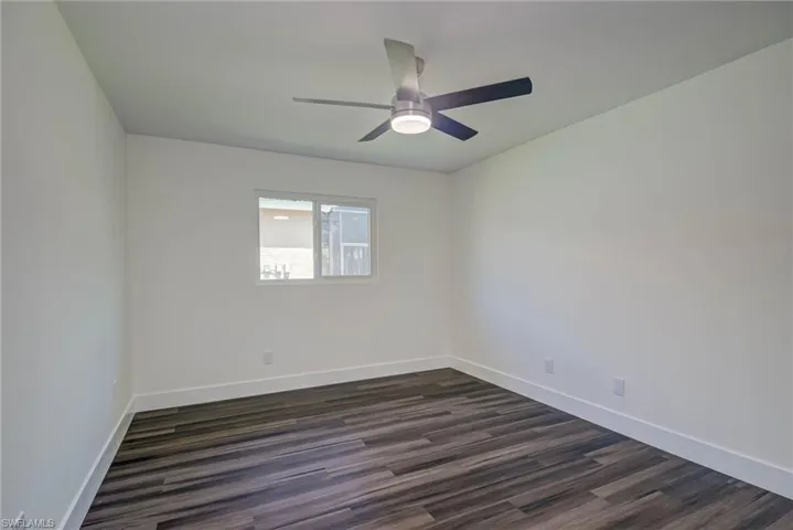 Empty room featuring baseboards, dark wood-type flooring, and a ceiling fan