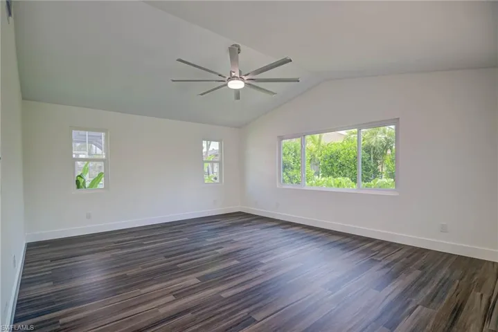 Empty room featuring lofted ceiling, ceiling fan, baseboards, and dark wood finished floors