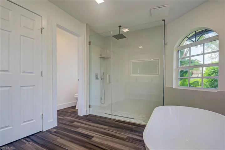 Bathroom with a stall shower, a soaking tub, wood finished floors, toilet, and baseboards
