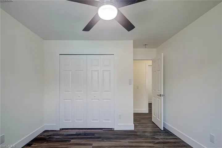 Unfurnished bedroom with baseboards, a closet, dark wood-style floors, and a ceiling fan