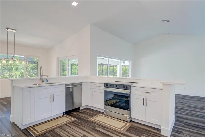 Kitchen featuring stainless steel dishwasher, electric range, a sink, vaulted ceiling, and a peninsula