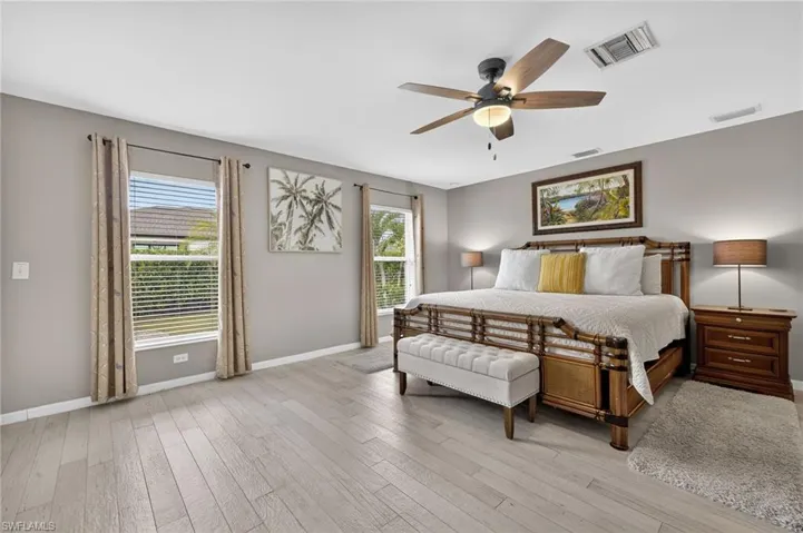 Generously sized guest bedroom with multiple windows for natural light, light wood-style flooring, and ceiling fan — comfortable accommodations in this fully furnished Cape Coral home.