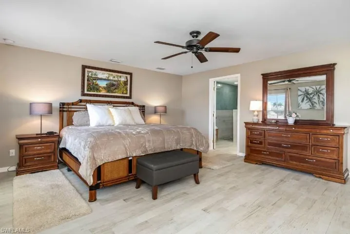 Primary bedroom suite with light wood-finish floors, ceiling fan, and direct ensuite bathroom access — a serene retreat in this Cape Coral turnkey pool home.