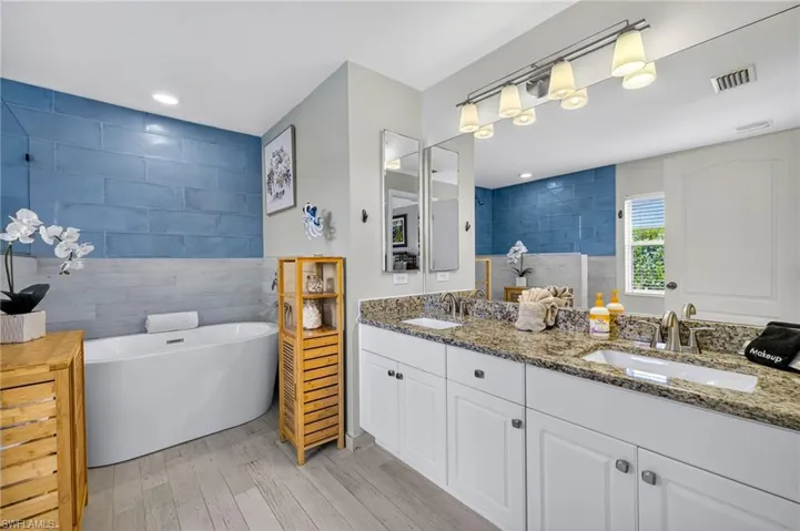 Luxurious primary ensuite bathroom featuring double vanity, soaking tub, walk-in shower, wood-style flooring, tile walls, and recessed lighting — a true spa retreat.