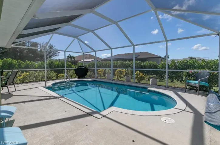 Sparkling in-ground pool surrounded by a spacious paver deck and full screened lanai enclosure — private, low-maintenance outdoor living at its best in Cape Coral, FL. Privacy hedges.
