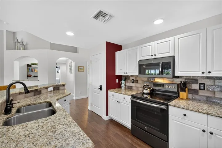 Updated kitchen with stainless steel appliances, arched walkways, decorative backsplash, white shaker cabinets, and dark wood-style tile flooring — a timeless design in this Cape Coral home.