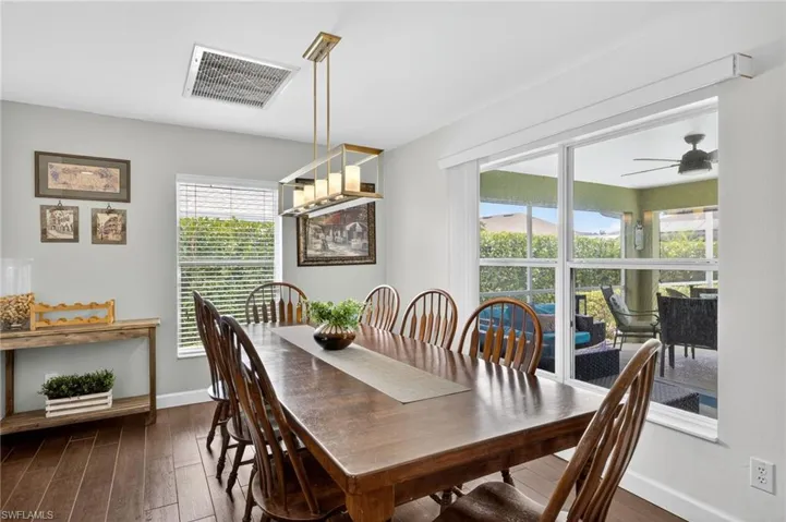 Formal dining room with dark wood-style flooring and ceiling fan — opens directly to the living area and kitchen, perfect for hosting family and guests in this Cape Coral turnkey home.
