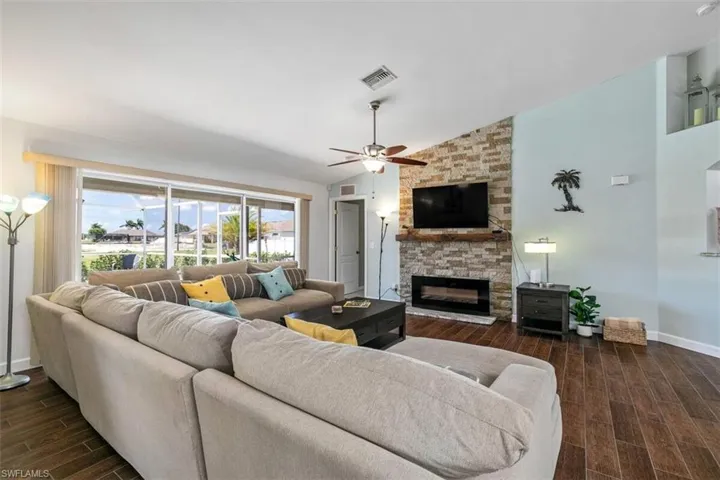 Open living room with wood-finish tile floors, stone fireplace, vaulted ceilings, and ceiling fan — warm and inviting in this Cape Coral furnished single-family home.
