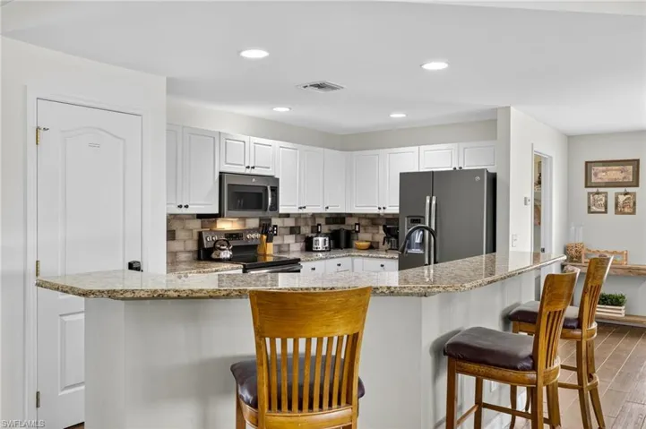 Chef's kitchen featuring granite countertops, stainless steel appliances, decorative tile backsplash, light wood-style flooring, recessed lighting, and breakfast bar seating.