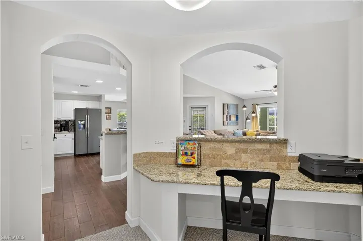 Sun-drenched kitchen with white cabinetry, stainless steel refrigerator, light stone countertops, and abundant natural light — bright and airy in this Cape Coral pool home.