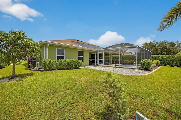 Rear exterior of 216 NW 29th Ave showcasing stucco siding, lush green lawn, screened lanai, and sparkling in-ground pool — a private Cape Coral backyard retreat.