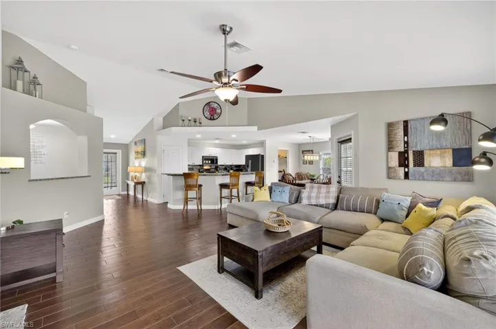 Spacious living room featuring vaulted ceilings, dark wood-style tile flooring, and ceiling fan — open-concept layout flows seamlessly to dining and kitchen areas at 216 NW 29th Ave.