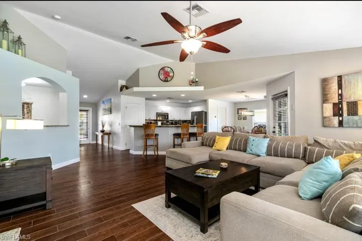 Elegant living room featuring arched walkways, soaring lofted ceilings, dark wood-style flooring, and ceiling fan — architectural details that set this Cape Coral home apart.
