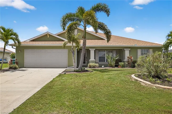 Attractive Cape Coral single-family home at 216 NW 29th Ave — stucco exterior, 2-car garage, concrete driveway, manicured tropical front lawn, and shingled roof. Turnkey and move-in ready.