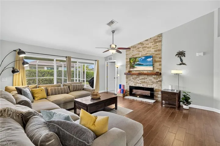 Elegant living area showcasing a decorative stone fireplace, soaring vaulted ceilings, dark wood-finish floors, and ceiling fan — a dramatic focal point in this Cape Coral pool home.