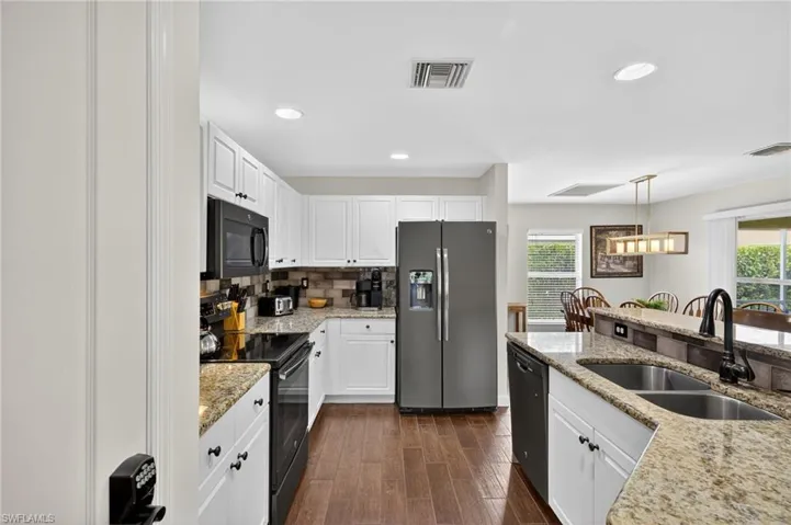 Well-appointed kitchen with black appliances, white cabinetry, granite-look countertops, decorative backsplash, dark wood-style floors, and recessed lighting throughout.