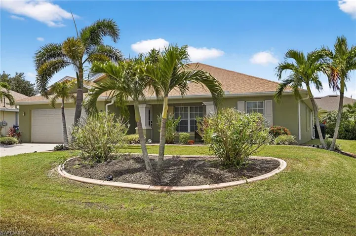 Stunning Cape Coral single-family home at 216 NW 29th Ave — single-story stucco construction with attached 2-car garage, lush tropical front lawn, concrete driveway, and classic shingled roof. Move-in ready and turnkey furnished.