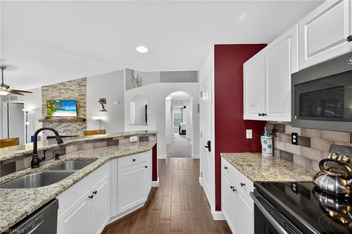 Spacious kitchen with black appliances, white cabinetry, ceiling fan, dark wood-style tile flooring, and recessed lighting — bright and functional in this NW Cape Coral pool home.