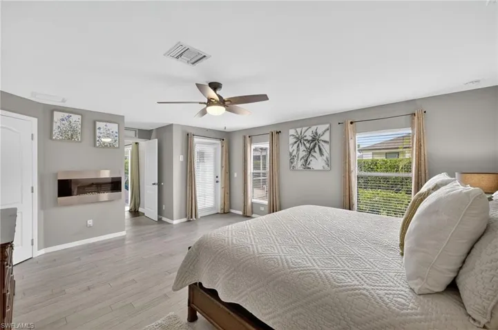 Bedroom with light wood-style floors, ceiling fan, and direct access to the screened lanai — ideal as a guest suite or flex room in this Cape Coral pool home.