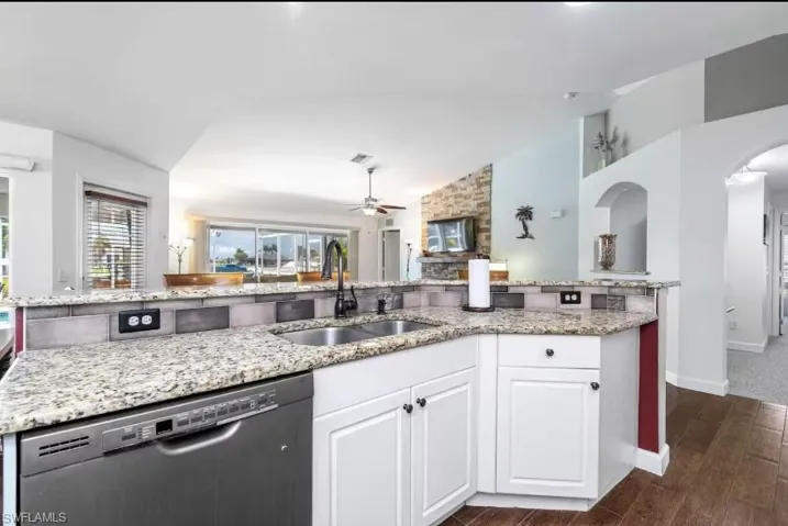 Open kitchen featuring stainless steel dishwasher, vaulted ceiling, ceiling fan, abundant natural light, and white cabinetry — airy and spacious at 216 NW 29th Ave.