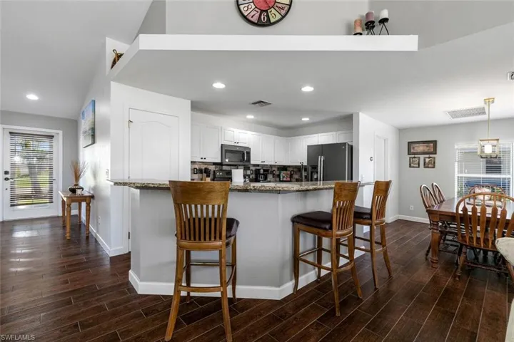 Well-equipped kitchen with stainless steel microwave, refrigerator with ice dispenser, white cabinetry, light stone countertops, and dark wood-style tile flooring.