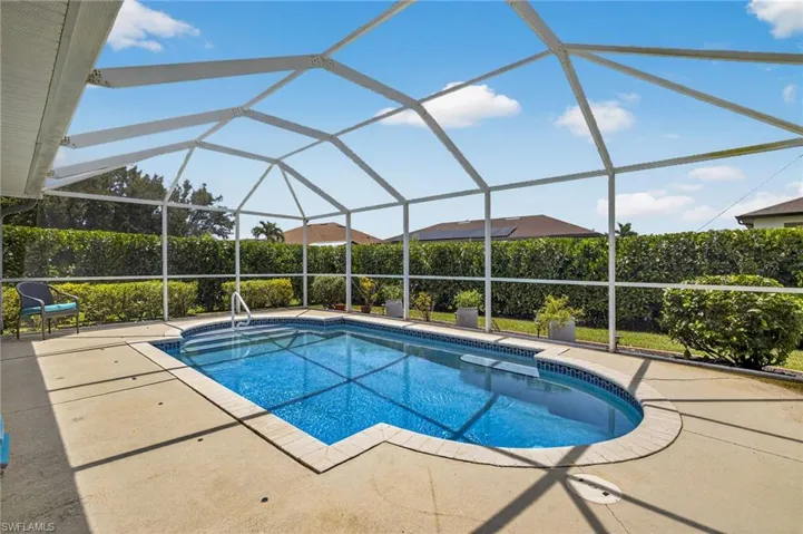 Solar-heated pool and screened lanai — a true backyard paradise featuring sparkling water, paver deck, and full screen enclosure for bug-free outdoor living in Cape Coral. Hedges to provide extra privacy.