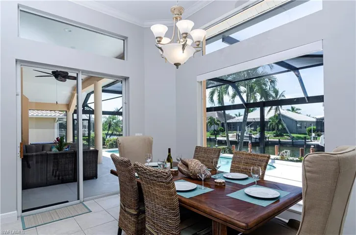 Dining space featuring ceiling fan with notable chandelier, a water view, ornamental molding, and light tile patterned floors