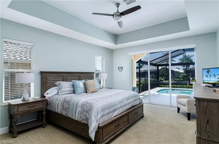 Carpeted bedroom with ceiling fan, a raised ceiling, and access to outside