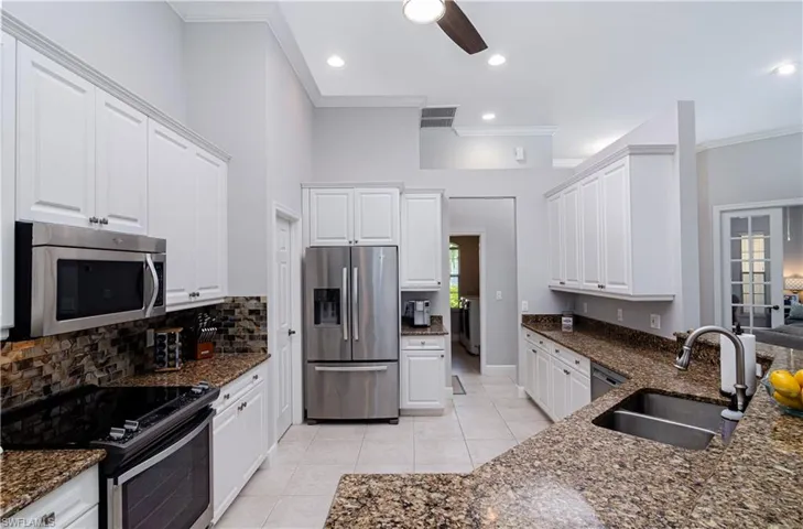 Kitchen with sink, light tile patterned floors, appliances with stainless steel finishes, white cabinetry, and dark stone countertops