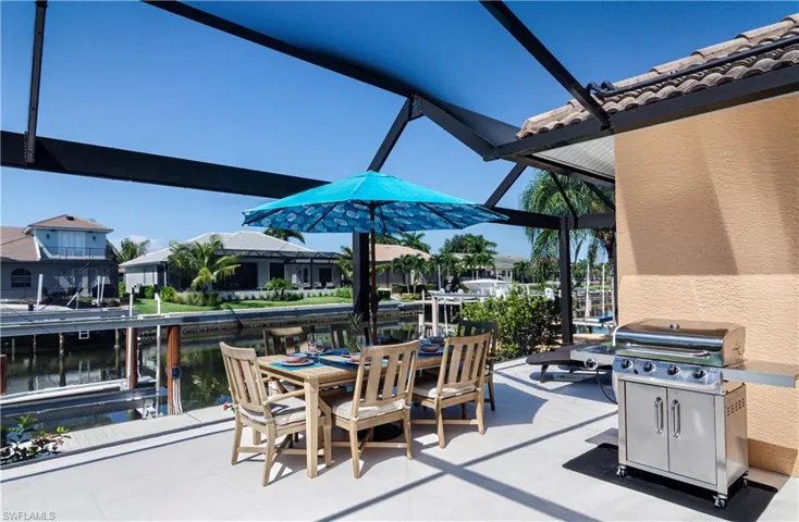 View of patio with area for grilling, a water view, and glass enclosure