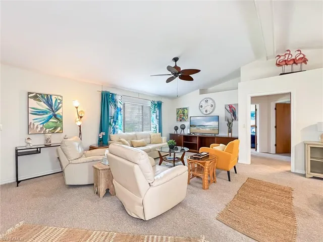Carpeted living room with vaulted ceiling with beams and ceiling fan