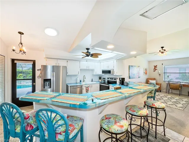 Kitchen featuring ceiling fan with notable chandelier, stainless steel appliances, white cabinetry, sink, and decorative backsplash
